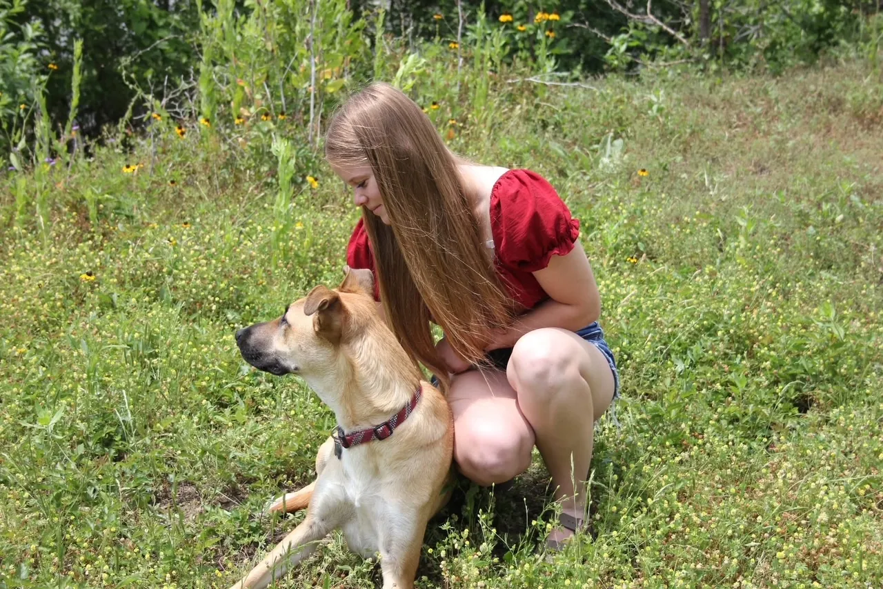 Skylar Beun crouched in a wildflower field beside a tan shepherd mix