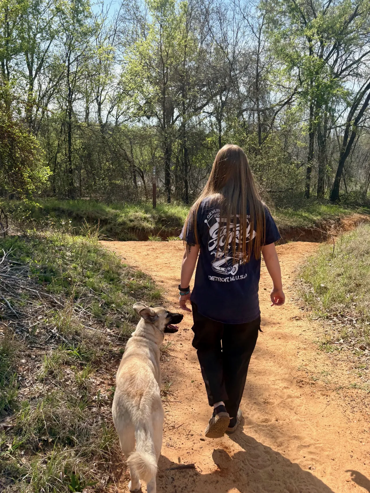 Trainer walking a cream-colored dog on a dirt trail through the woods